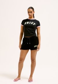 T-shirt noir court avec des accents roses et "JUICY" en lettres vertes, associé à un short noir portant le même logo et des tongs roses.