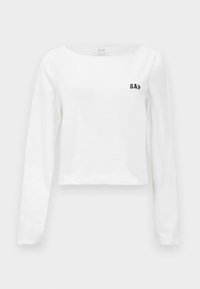 Bílé dlouhé rukávy crop top s lodičkovým výstřihem a malým černým logem "GAP" na levé části hrudníku.