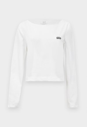 White long-sleeve crop top with boat neckline and small black "GAP" logo on left chest.