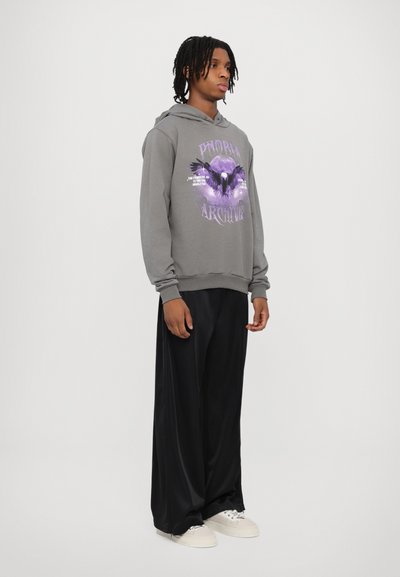 Felpa grigia con un design grafico e accenti viola, abbinata a pantaloni neri a gamba larga e sneakers bianche. Stile semplice e contemporaneo.
