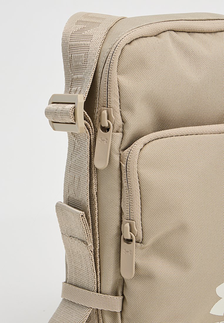 Sac à dos en tissu beige avec une sangle texturée, des fermetures à double zipper et une poche latérale. Design structuré pour un usage fonctionnel.