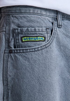 Zbliżenie na kieszeń jasnoniebieskich dżinsów z małą zielono-niebieską naszywką z logo DC Shoes.