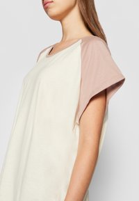 Kortärmad topp i krämfärg och mjuk rosa, med rundad halsringning och lös passform, tillverkad av mjukt bomullsmaterial med en slät yta.