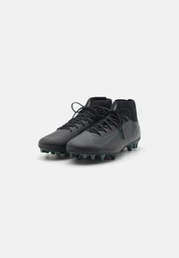 Bottes de football noires avec une tige synthétique texturée, des lacets plats et un col haut. La semelle présente plusieurs crampons pour l'adhérence.