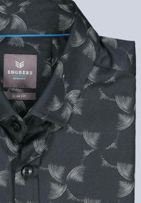 Schmal geschnittenes Hemd aus schwarzem Stoff mit einem Wellenmuster in Off-White. Mit Kragen und schwarzen Knöpfen vorne. Markenlabel: Engbers.