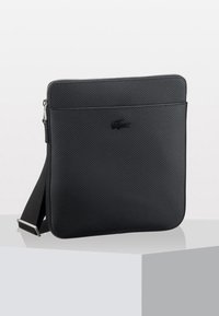 Borsa a tracolla nera con superficie texturizzata, chiusura con zip e tracolla regolabile. Presenta un discreto logo sul davanti. Forma rettangolare.
