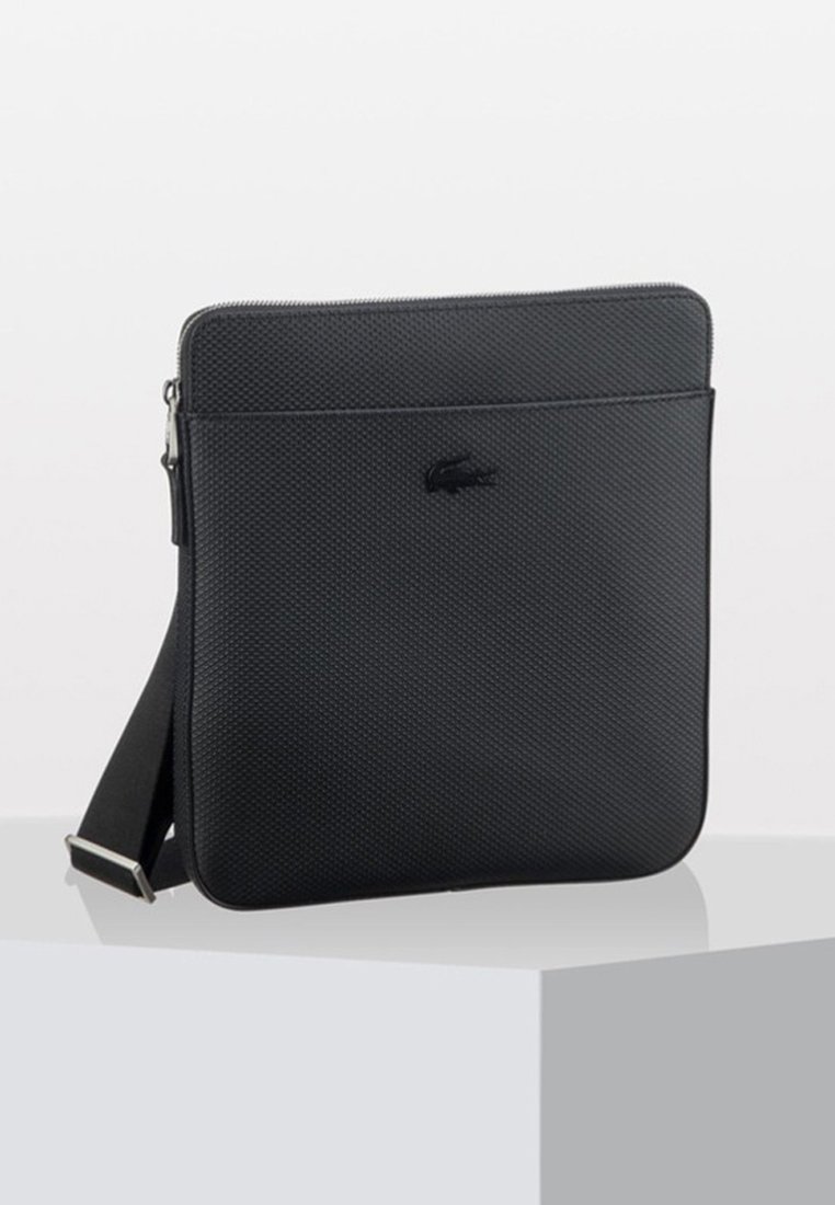 Borsa a tracolla nera con superficie texturizzata, chiusura con zip e tracolla regolabile. Presenta un discreto logo sul davanti. Forma rettangolare.