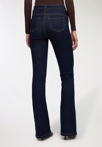 Ciemnoniebieskie dżinsy o rozszerzanym kroju i wysokim stanie, wyposażone w dwie tylne kieszenie oraz widoczne akcenty szwów. Tkanina wydaje się gładka i strukturalna.