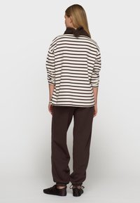 Pasiasty, oversize sweter w kolorze kremowym i brązowym, z miękkim kołnierzem. W połączeniu z ciemnobrązowymi spodniami dresowymi i czarnymi butami na sznurówki.