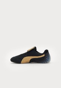 Black sneaker with gold accents, textured upper, lace-up design, and an icy blue translucent sole with rounded nodules on the heel.
