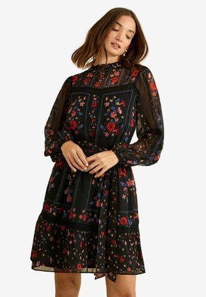 Rochie neagră cu imprimeu floral, mâneci lungi diafane, guler înalt, tiv în straturi, cu modele florale roșii, albastre și galbene și accente de dantelă.