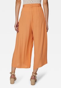 Lichte, soepele culottes tot op de knie in een effen apricot-kleur met een riem in de taille. Heeft een textuurafwerking en een wijde, relaxte pasvorm.