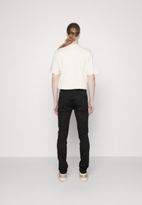 Schwarze Jeans im Slim-Fit-Stil, kombiniert mit einem cremefarbenen T-Shirt. Das Outfit wird durch hellfarbene Sneaker ergänzt. Schlichtes Design und minimale Details.
