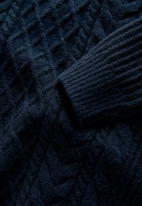 Marineblauer gestrickter Pullover mit einem strukturierten Zopfmuster, ausgestattet mit gerippten Bündchen und einer weichen, flauschigen Textur. Nahaufnahme der Stoffdetails.