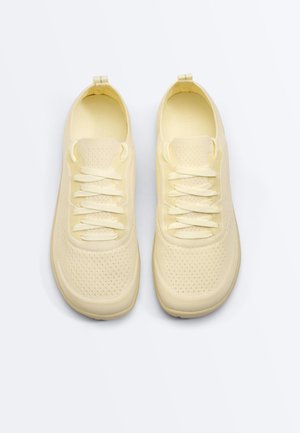 Pair of lightweight, pale yellow knit sneakers with textured soles and matching laces, shown from above on a white background.