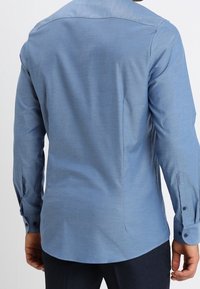 Lichtblauw overhemd met lange mouwen, gestructureerde stof, puntkraag, geribde manchetten met knopen, achterkant met inzetstuk, getailleerde pasvorm, strakke lijnen zonder logo's.