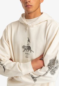 Cream hoodie with graphic prints of a tiger, bird, and palm tree. Features drawstring hood and ribbed cuffs. Soft cotton material.