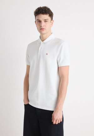 Witte polo met korte mouwen en een puntige kraag, met een klein rood logo op de linkerborst en een zachte, gestructureerde stof.