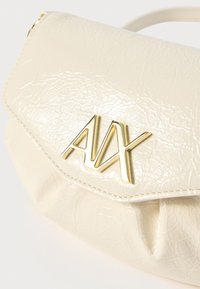 Kreemitooni sünteetilisest nahast käekott, millel on kortsunud tekstuur, esiküljel kuldne "A|X" logo ja turvaline klappi süüdmise mehhanism.