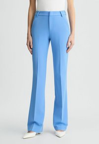 Pantaloni blu su misura con una texture liscia, vestibilità adattata, parte anteriore piatta e tasche, abbinati a scarpe bianche a punta.