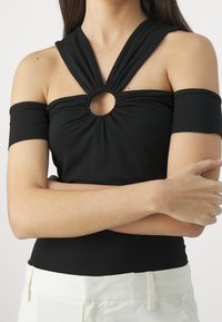 Top negro sin hombros con un diseño en torsión, que presenta un corte circular en el centro y una tela elástica. Combinado con pantalones de color claro.