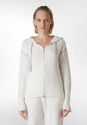 White zip-up hoodie with a hood, made of soft material, featuring gray drawstrings and side pockets, worn over matching white bottoms.
