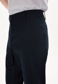 Mörkblå byxor i ett mjukt tyg, med knappstängning och hällor för bälte, skräddarsydd passform och sidofickor.