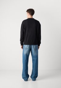 Felpa nera con collo a giro e polsini a costine, abbinata a jeans di denim azzurri chiari, morbidi e con tasche posteriori e un finish sbiadito.