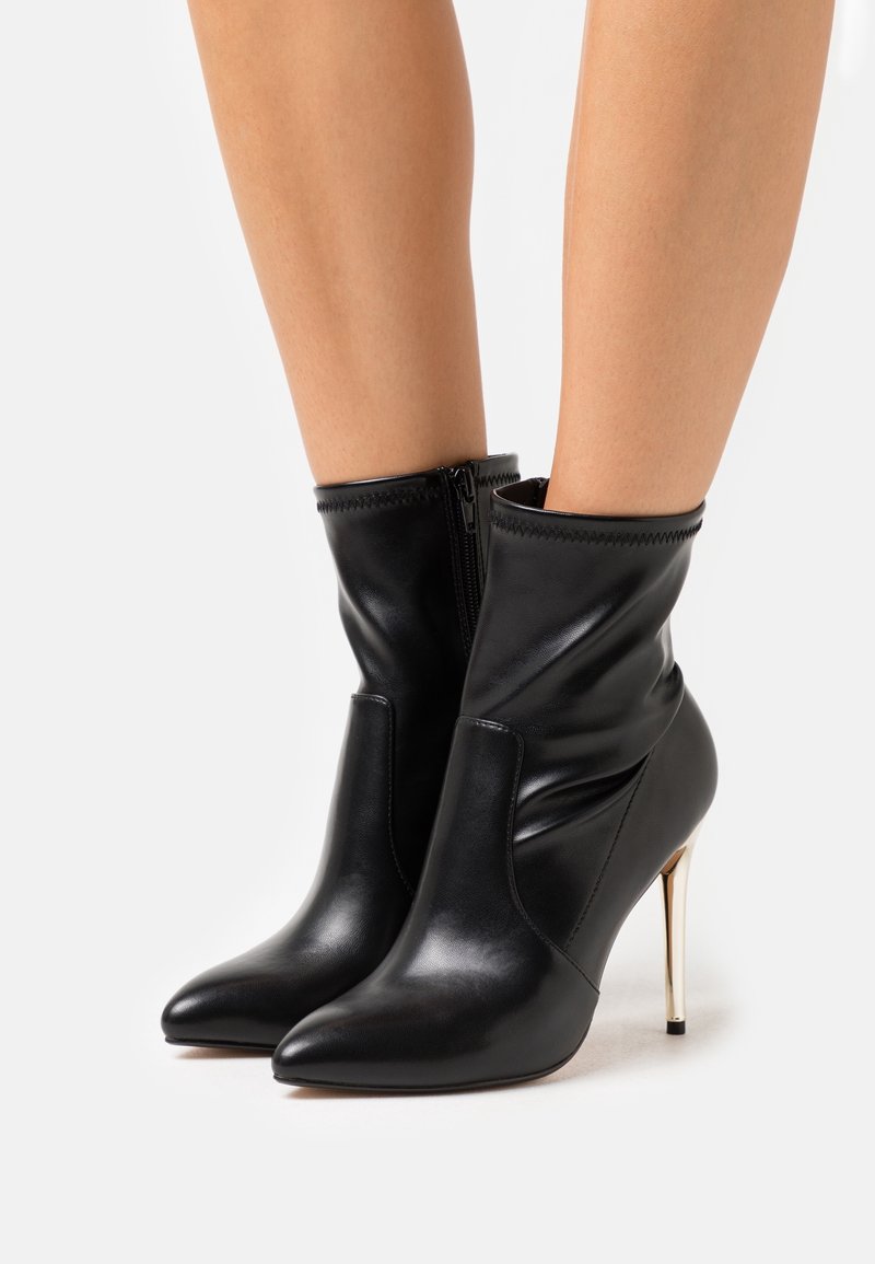 Bottines en cuir noir avec tige souple, bout pointu et talon aiguille doré. Dotées d'une fermeture éclair latérale. Texture lisse.