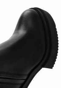 Black leather ankle boot with a rounded toe and textured sole. Features stitched detailing and a slightly raised heel.
