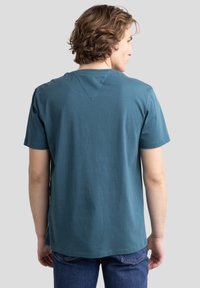 Kratkām piedurknēm t-krekls no zaļgana kokvilnas ar apaļu kaklu un bezšuvju muguru. Iespējams, diskrēta V veida detaļa kakla zonā.