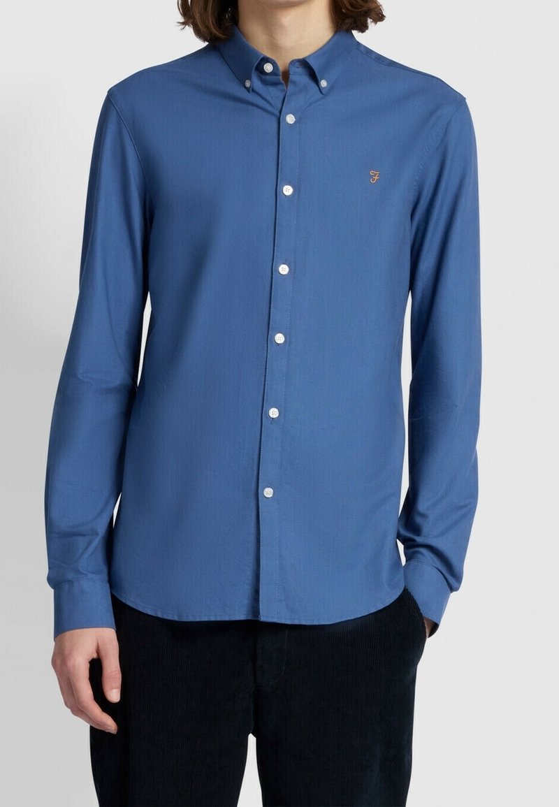 Camicia a maniche lunghe con bottoni in tessuto blu uniforme, dotata di colletto button-down, bottoni bianchi e un piccolo logo sul lato sinistro del petto.