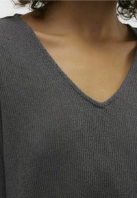 Maglione grigio a maglia con scollatura a V e materiale testurizzato, messo in risalto da un motivo a coste. Vista ravvicinata che evidenzia l'area della scollatura.