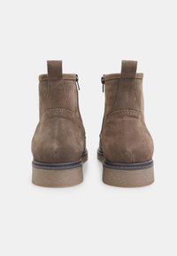 Botine din suede maro, cu o textură netedă, două fermoare laterale și o talpă din cauciuc negru, cu striuri orizontale subtile.