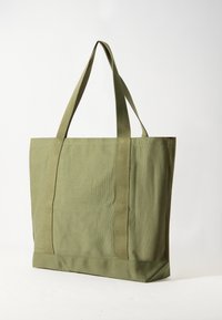 Zöld vászontáska két hosszú füllel, téglalap alakú, texturált anyagból készült, és merev alappal rendelkezik.