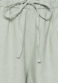 Pantalon en lin vert clair avec taille à cordon, surface texturée et coupe ample pour plus de confort.