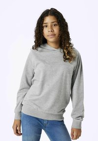 Haut de survêtement gris en tissu doux, avec une poche kangourou, un ourlet arrondi et des manches longues. Porté avec un jean bleu.