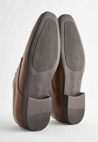 Chaussures habillées en cuir marron avec semelles en caoutchouc, présentant une finition lisse, un bout arrondi et un motif de sculpture texturé sur les semelles.