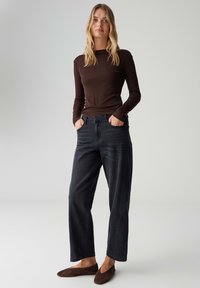 Bruine top met lange mouwen, zwarte rechte jeans en bruine suède ballerina's. Eenvoudig design, nauwsluitende top, gestructureerde stof, casual stijl.