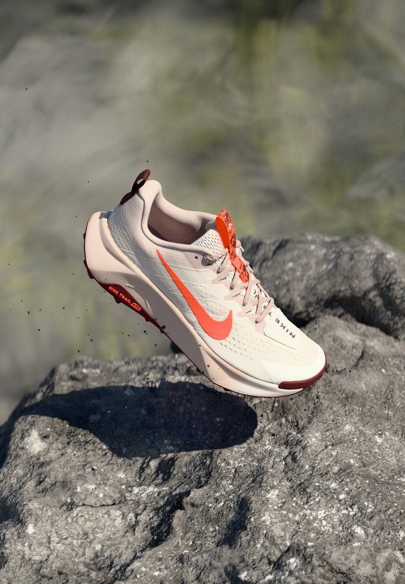 Light beige running shoe with orange accents, textured upper, and a supportive heel. Red outsole with traction lugs for grip on various surfaces.