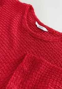 Rød tekstureret bluse med en vaffel-lignende design, rund halsudskæring og korte ærmer. Etiketten viser mærket "NEXT."