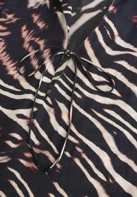 Tissu foncé avec un motif zébré de tigre dans des nuances de noir, blanc et marron, présentant un décolleté en V et une fermeture à nouer au niveau du cou.