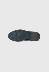 Sola de sapato de couro preto com um padrão de aderência texturizado, incluindo sulcos e uma secção lisa. Apresenta um bico arredondado e um salto plano.