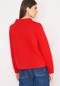 Czerwona bluza z kołnierzem, wykonana z miękkiego materiału, z elastycznymi mankietami. Połączona z denimem, prezentuje casualowy, swobodny krój.