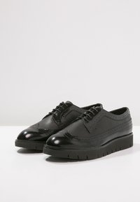 Chaussures en cuir noir à finition lisse, avec un design à bout golf et des détails perforés. Dotées d'une semelle épaisse et texturée pour un surcroît de hauteur.