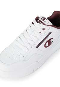 Weiße Sportschuhe aus strukturiertem Leder, mit perforierter Zehenkappe und burgunderfarbenem Logo sowie Akzenten. Mit flachen Schnürsenkeln und gepolstertem Schaft.