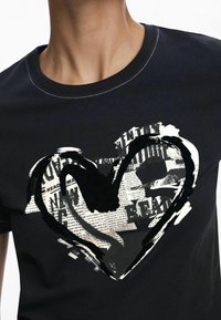 Černé bavlněné tričko s velkým srdcem s novinovým vzorem v bílé a černé, se kulatým výstřihem a krátkými rukávy.