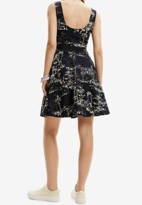 Robes noires avec imprimé floral beige, corsage ajusté, jupe évasée, dos dégagé, fabriquée en tissu respirant ; associée à des baskets légères.