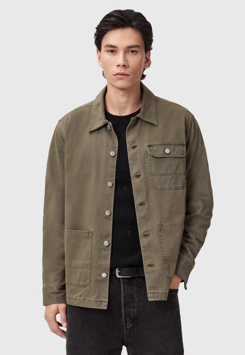 Giacca verde oliva chiaro in cotone, con chiusura a bottoni, due tasche frontali e colletto all'italiana. Finitura in tessuto testurizzato.