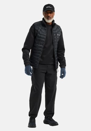 Gilet nero imbottito sopra un felpa nera, pantaloni cargo neri, guanti blu e sneakers neri. Include un cappellino nero con logo bianco.